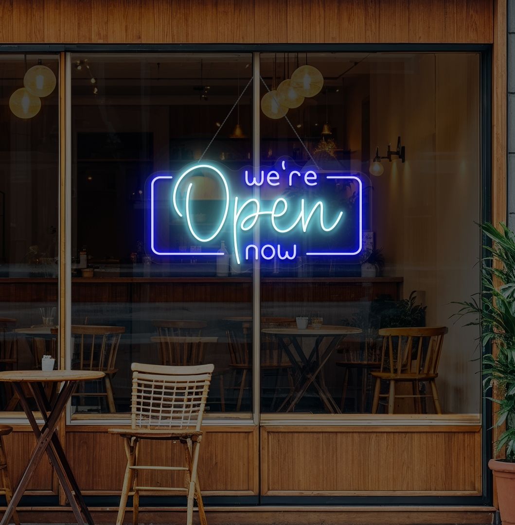 Image of a "We're open now" neon sign glowing on a cafe glass door in ice blue color.