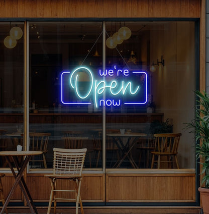 Image of a "We're open now" neon sign glowing on a cafe glass door in ice blue color.