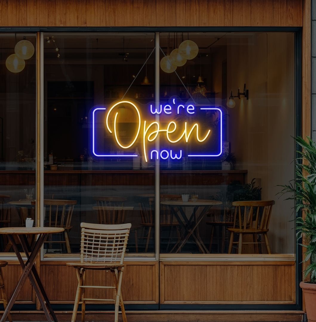 Modern we're open now neon sign glowing orange on cafe door.