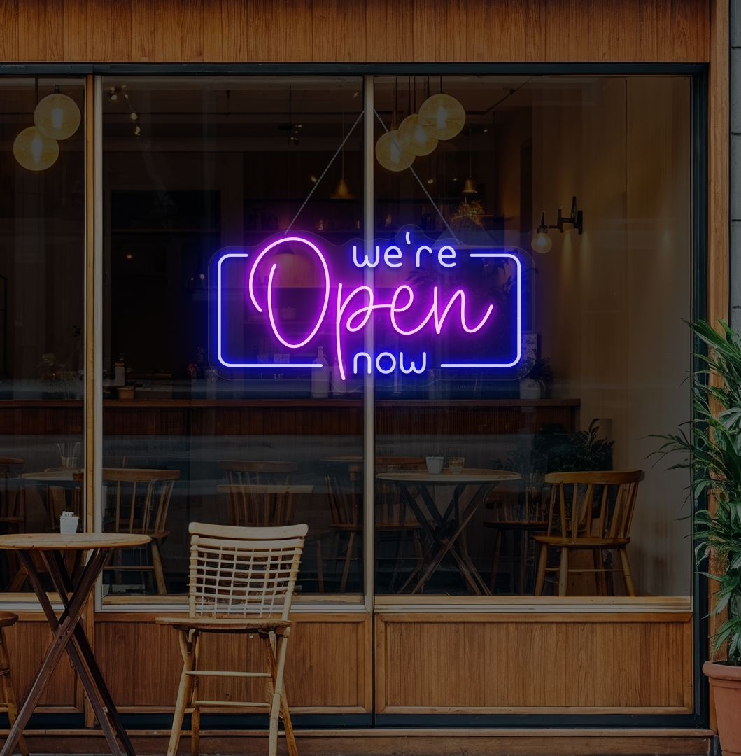 Modern we're open now neon sign glowing purple on cafe door.