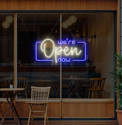 Modern we're open now neon sign glowing warm white on cafe door.