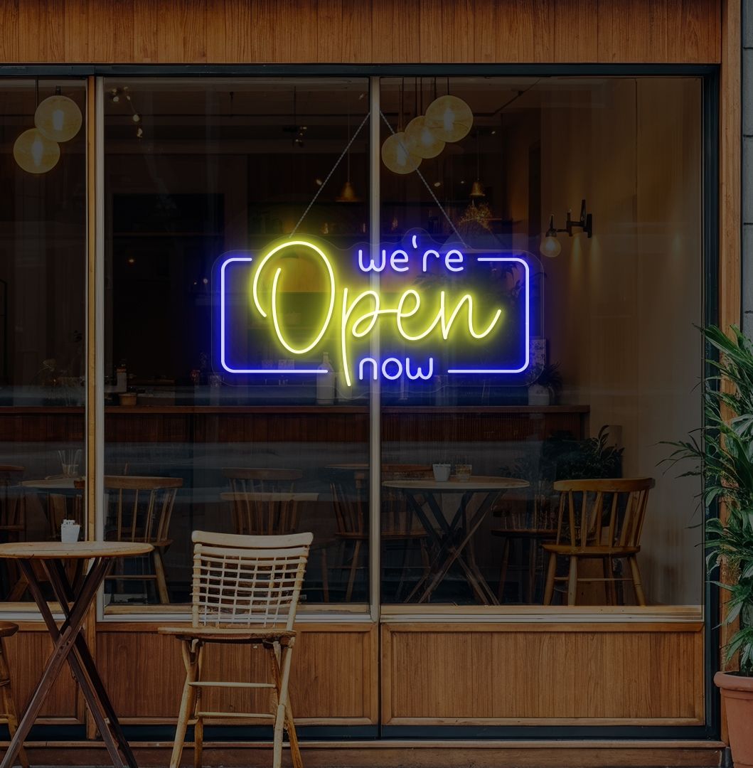 Modern we're open now neon sign glowing yellow on cafe door.