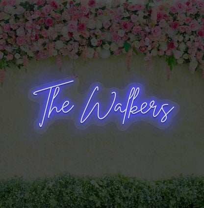 Personalized wedding name neon sign glowing blue on wedding backdrop.