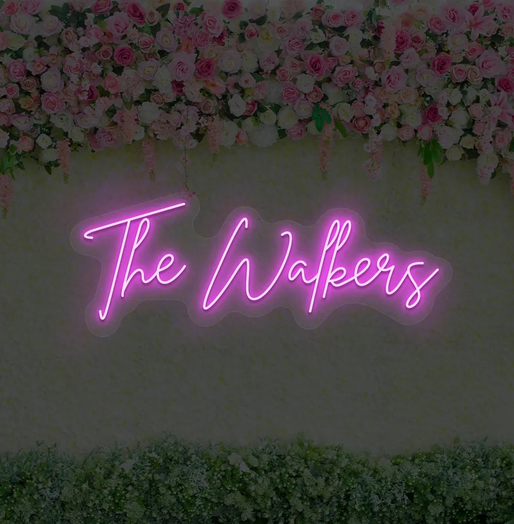 Personalized wedding name neon sign glowing pink on wedding backdrop.