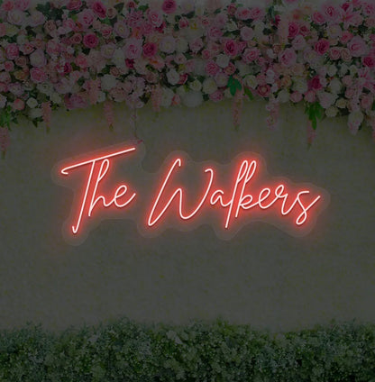 Personalized wedding name neon sign glowing red on wedding backdrop.