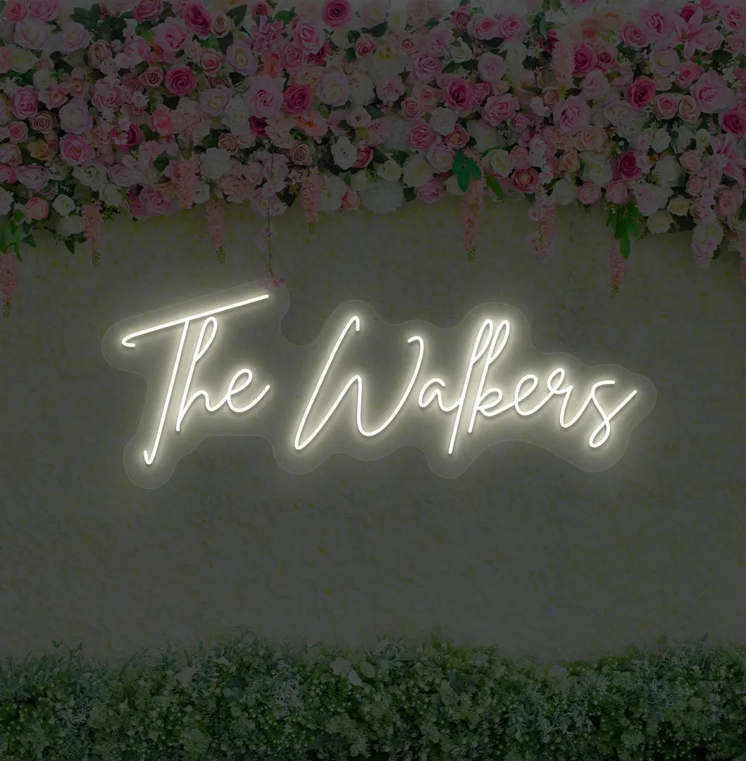 Image of a wedding name neon sign glowing warm white on decorative wall.