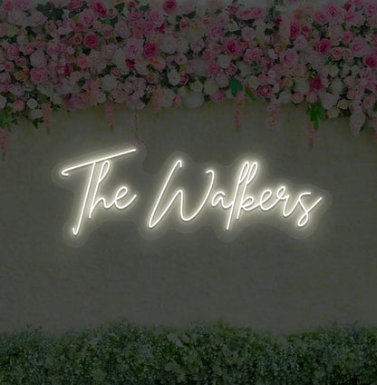 Image of a wedding name neon sign glowing warm white on decorative wall.