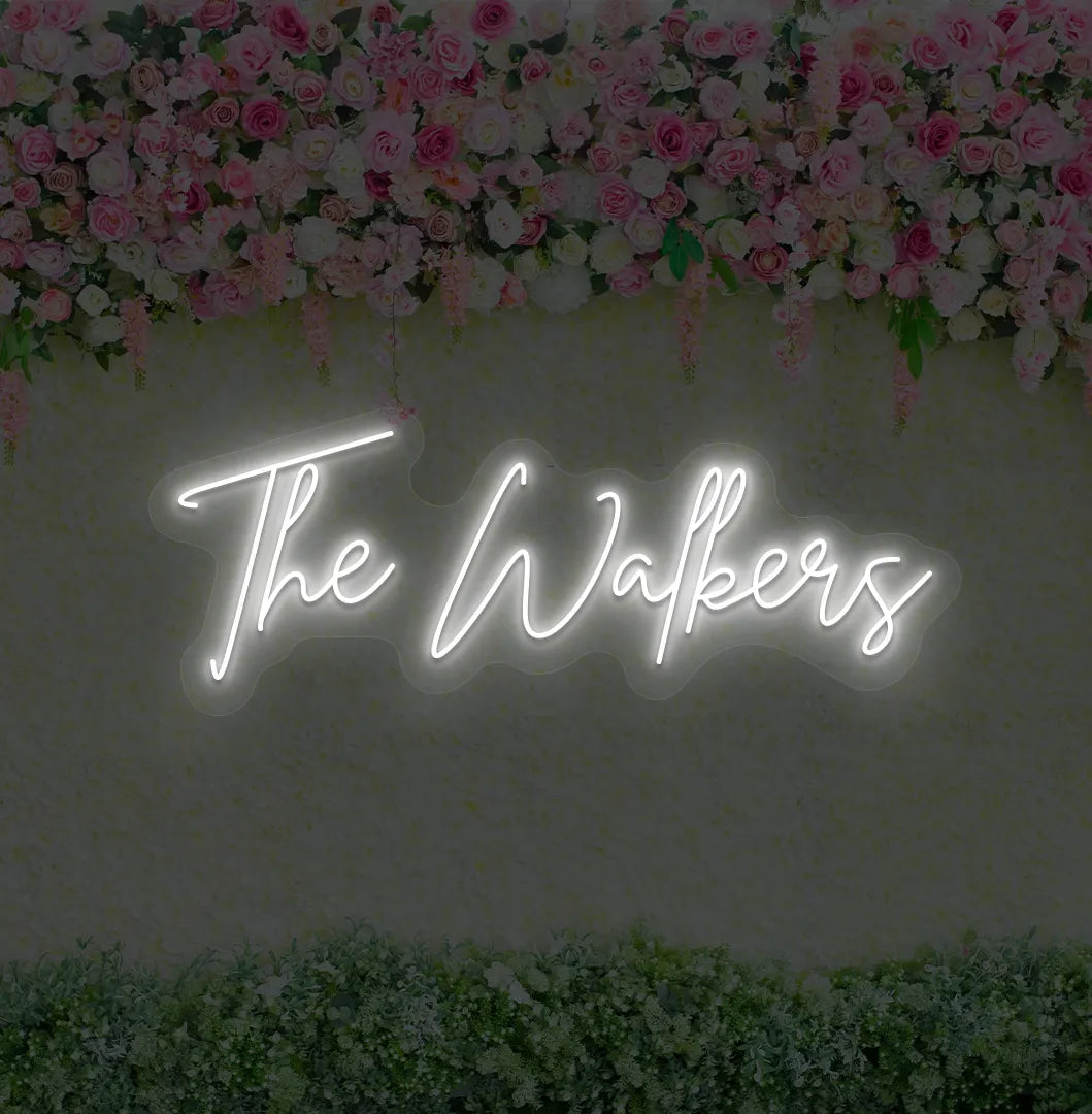 Personalized wedding name neon sign glowing white on wedding backdrop.