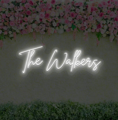 Personalized wedding name neon sign glowing white on wedding backdrop.