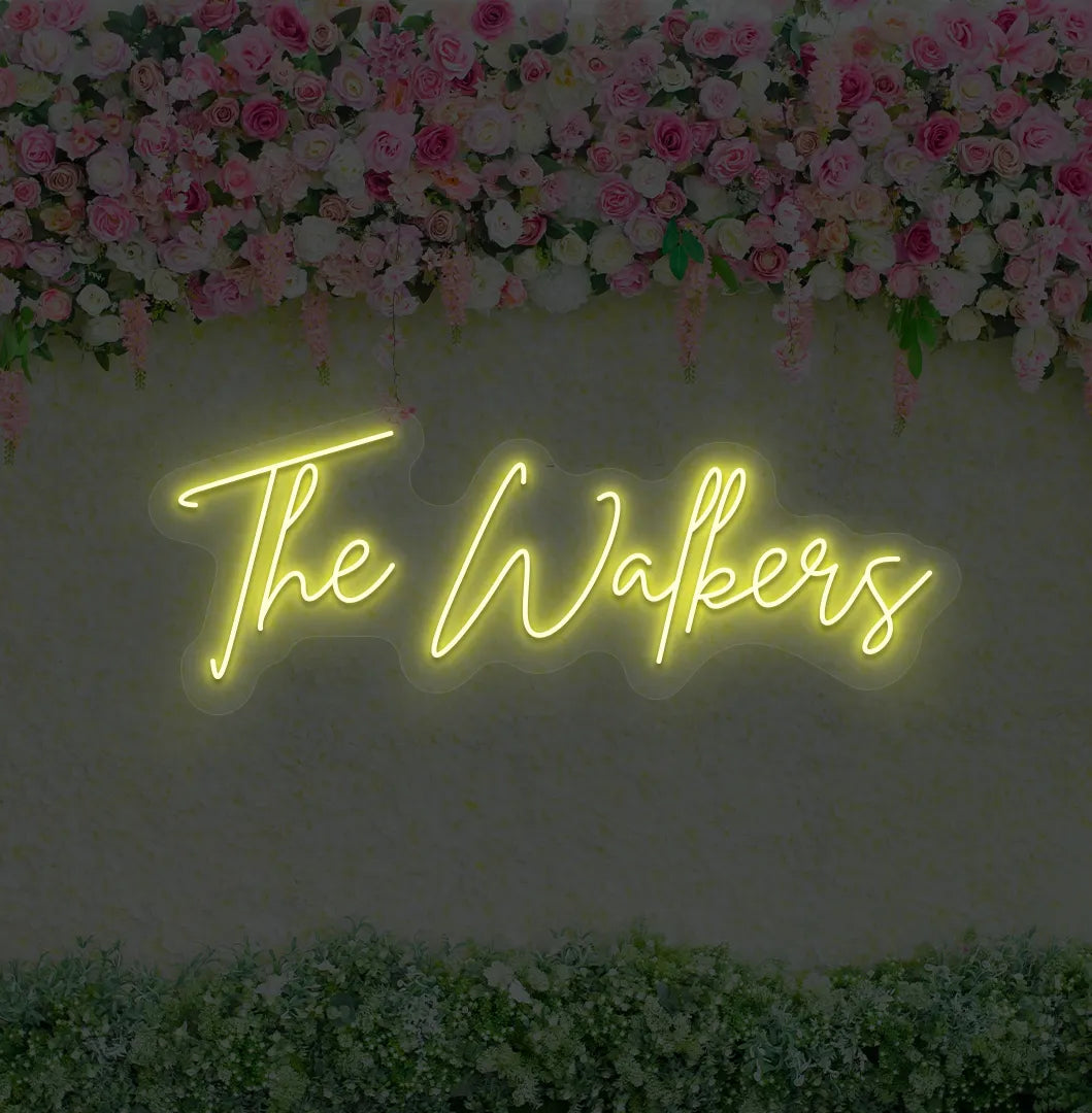 Image of a wedding name neon sign glowing yellow on decorative wall.