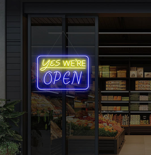 Image of a "Yes, we're open" neon sign glowing on a cafe glass door in blue color.