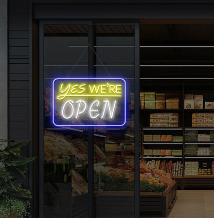 Image of a "Yes, we're open" neon sign glowing on a cafe glass door in white color.