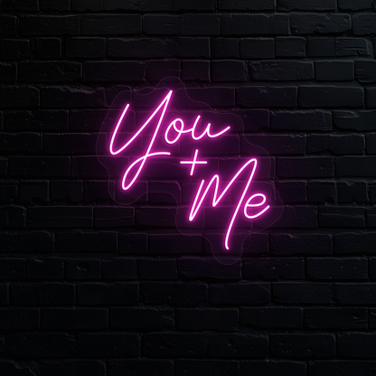 Image of a "you plus me" LED neon sign glowing on wall in pink.